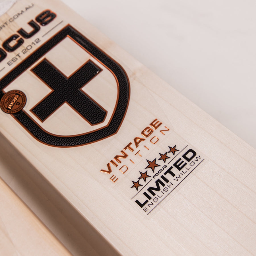 A premium-grade cricket bat from Focus, displayed from three different angles – front, back, and side view. The bat features a light-colored willow blade with a sleek design, bold focus cricket branding